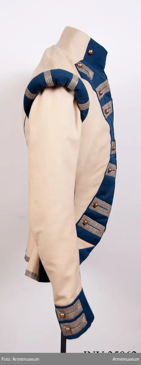 Rekonstruktion av jacka m/1781 för officer vid Lätta livdragonerna.
Jackan är sydd av vitt kläde med kragspeglar, bröstrevärer, axelkarmar och ärmuppvik i mörkblått kläde. Passpoaler av blått kläde i ryggsömmar och främre delsömmar på ärmarna.
Den är dekorerad med metallgaloner på bröstrevärer, axelkarmar och ärmuppslag, och har 16 icke funktionella kulknappar av mässing fram, samt 2 i varje ärmslut och 2 vid ryggslutet bak.
Mitt-fram-linjen är kraftigt svängd, och framstyckena är vadderade över bröstet. Jackan stängs mitt fram samt i ärmsprunden med hysk och hake. 
Den är konstruerad med avskärning i midjan, samt insnitt fram. Separata sidstycken. Skört utan slits bak.
Axelkarmarna är vadderade och står rakt upp.
Jackan är helfodrad med vitt bomullstyg.

Plaggets skärning och sömmar, de vadderade axeltungorna, de djupt skurna bröstrevärerna, uppviken, fodret m.m. indikerar ganska tydligt att den är tillverkad senare, troligen under sent 1800-tal. Även tygkvalitéerna indikerar en yngre datering. 

Grupp C I.