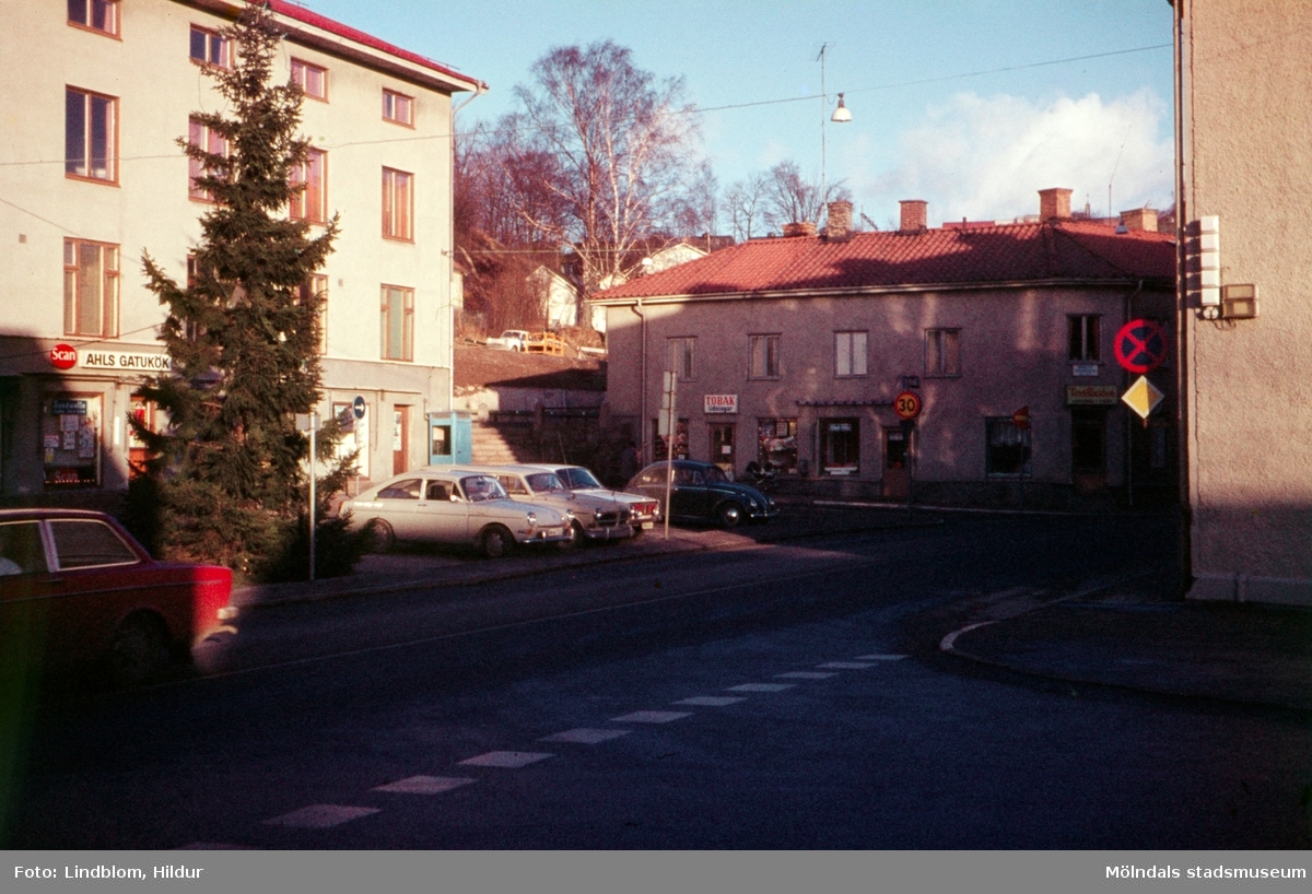 Gamla Torget i Mölndal, 1970-tal. Till vänster ses Kvarnbygatan 43 och till höger Kvarnbygatan 45. En gran är placerad på torget där även bilar står parkerade.

För mer information om bilden se under tilläggsinformation.
