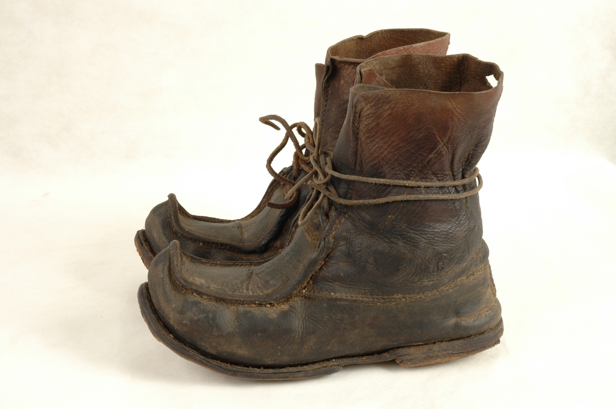 Et par sko av samisk type. Alt i lær. Skinnreimer til knytting rundt ankel. Liten dekor preget inn i læret på oversiden av skoen og bokstavene F L.