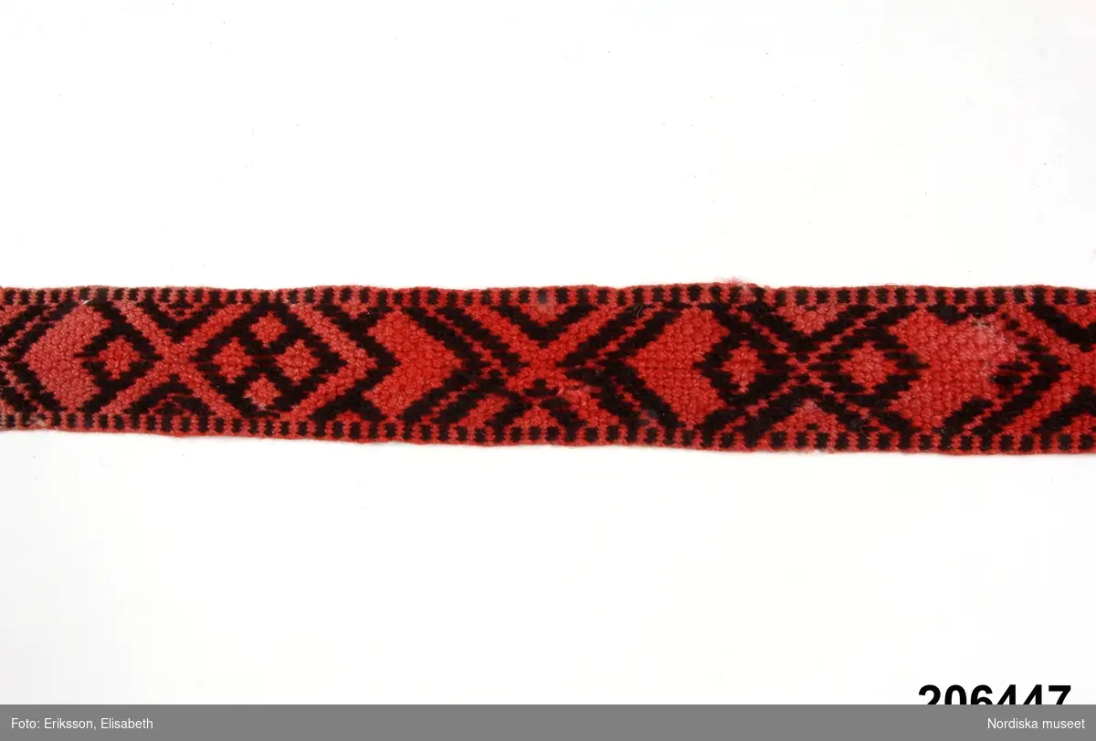 Band vävt i bandsked av  rött och natursvart ullgarn med  geometriskt mönster, använt som barnlinda. 
 /Berit Eldvik 2013-02-13