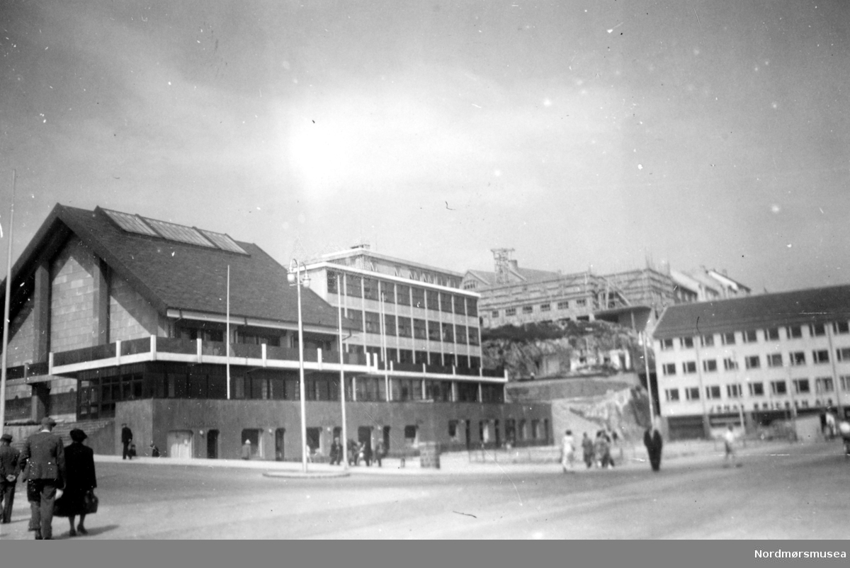 På bildet ser vi Kaibakken, Rådhuset (med adressen Kaibakken 2) og Rådhus-plassen (tidligere Fisketorget) fra venstre til midt på bildet. Ellers midt på bildet i bakgrunnen, ser vi Hotell Fosna under bygging, og til høyre ser vi Jonas Eriksens butikklokaler. Bildet er datert Juni 1953. Nordmøre Museums fotosamling 