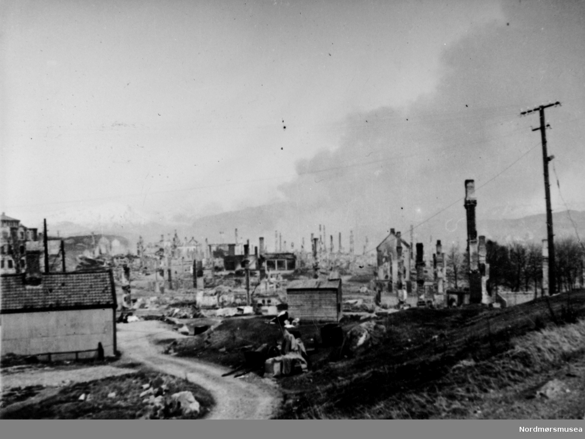 Krigen har kommet til Kristiansund. Etter nazistenes herjinger i perioden 28. april til 1. mai 1940 ligger store deler av byen i ruiner.

Etter bombigen løp det totale antall brente bygg på tilsammen 767, hvor 605 av disse var på Kirkelandet og 162 på andre ";land"; i Kristiansund. Her fantes det til blant annet til sammen 3906 boliger ifølge boligtellingen av 1938, og av disse brant 2162 boliger ned og 7099 mennesker ble husløse. I tillegg til de 767 brente byggene brant 36 fiskepakkehus ned til grunnen, hvorav 34 lå på andre ";land";. Verdien av de brente byggene beløp seg til kroner 26,9 millioner for Kirkelandet (kroneverdi per 1940) eller tilsammen 30,6 millioner kroner (kroneverdi per 1940) for hele byen. Fra Nordmøre Museums fotosamlinger. Kilde: Gjenreisningsproblemer i Kristiansund. Fremlagt ved gjenreisningsinstituttet i Kristiansund. Juli 1945. Side 16 - 20.

