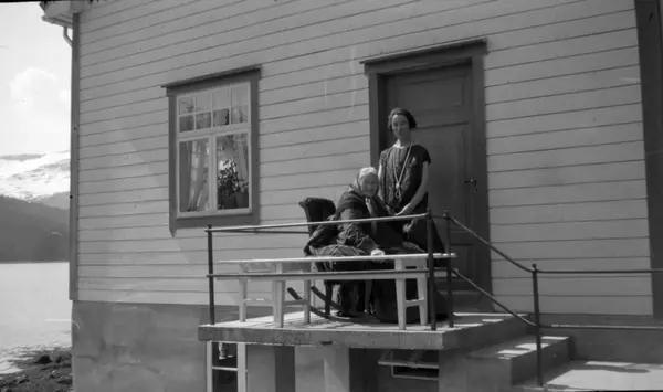 Foto av to kvinner, hvorav den ene sitter i gyngestol. Kvinn