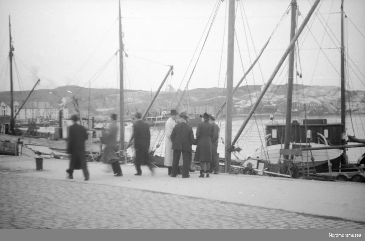 Foto fra gjenreisningsbyen Kristiansund, hvor vi ser fra Vågekaia med fiskebåter fortøyd. Datering er trolig omkring 1940 til 1950. Fotograf er ukjent. I bakgrunnen ses Gomalandet.  Fra Nordmøre museums fotosamlinger.