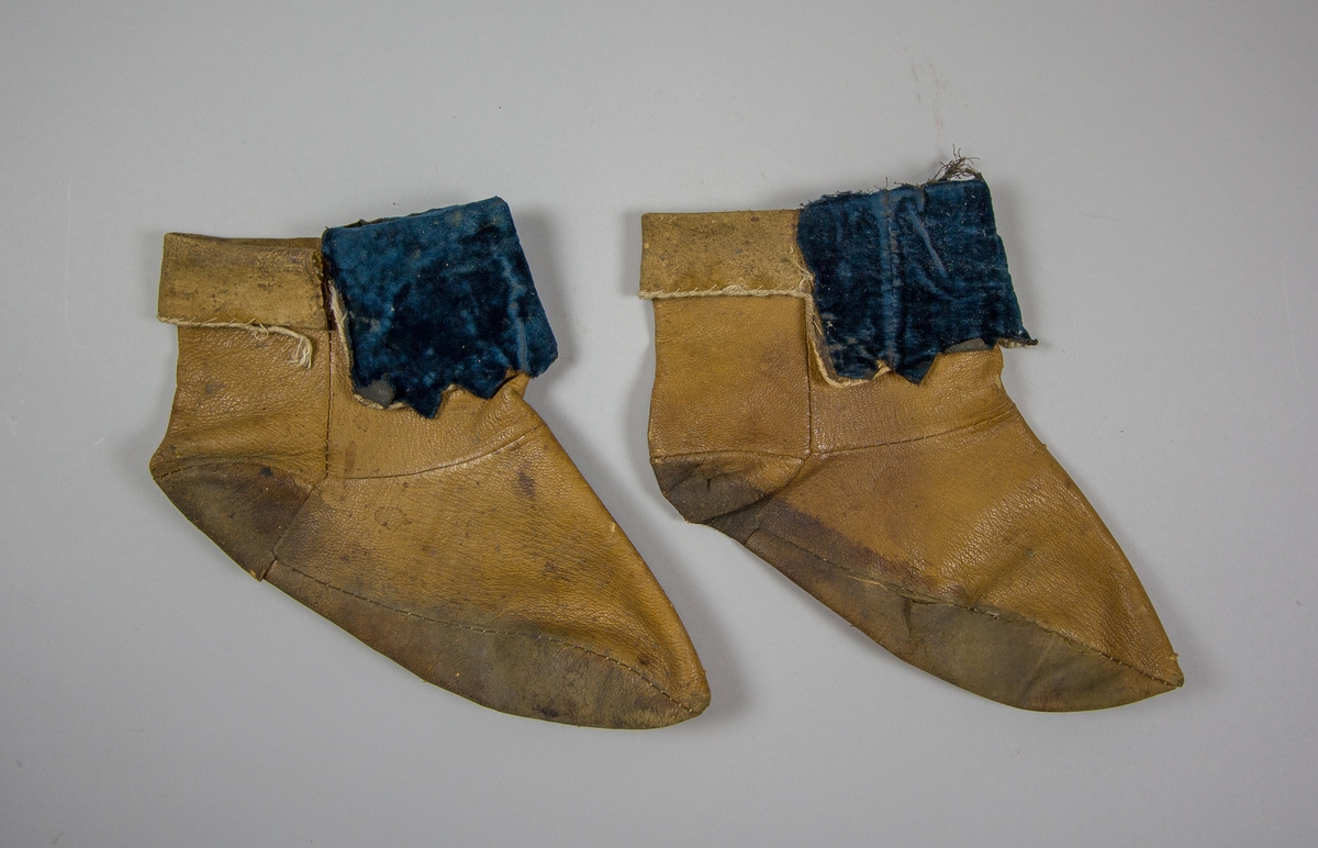 Skor, 1 par, av brunt läder som går upp över vristen, sammanfogade av flera delar. Påsydd dekoration av blå sammet på den nedvikta kanten.