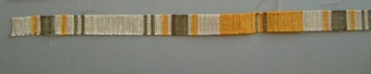 Väven har namnet TUSSILAGO. Kerstin Brandt, Äppelbo - vävde 28,75 m á 9:- 1979. Provet är vävt i tuskaft medcottolin 28/2 i varpen och inslag av lingarn nr 12. Löparen är randig i vitt, grått och gult.