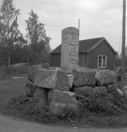 Foto av en milsten av sten (granit) med röse och text:  "Karlshamn 35, Tingsryd 10 , Växjö 53 Km , Urshult 13 Km."
9600 m S, 18 ° V om Tingsås kyrka. 1 m NV om vägen i skälet mellan vägen till Karlshamn och vägen till Urshult. 
Vägen Kvarnamåla-Gäddeviksås-Karlshamn. 
Källa: Kronobergs läns väginventering 1943.