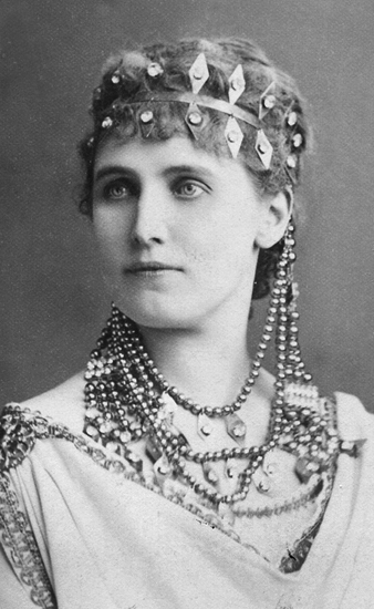Rollporträtt av Christina Nilsson. Hon bär klänning, många pärlhalsband samt ett diadem. Helena ur operan Mefistofeles.