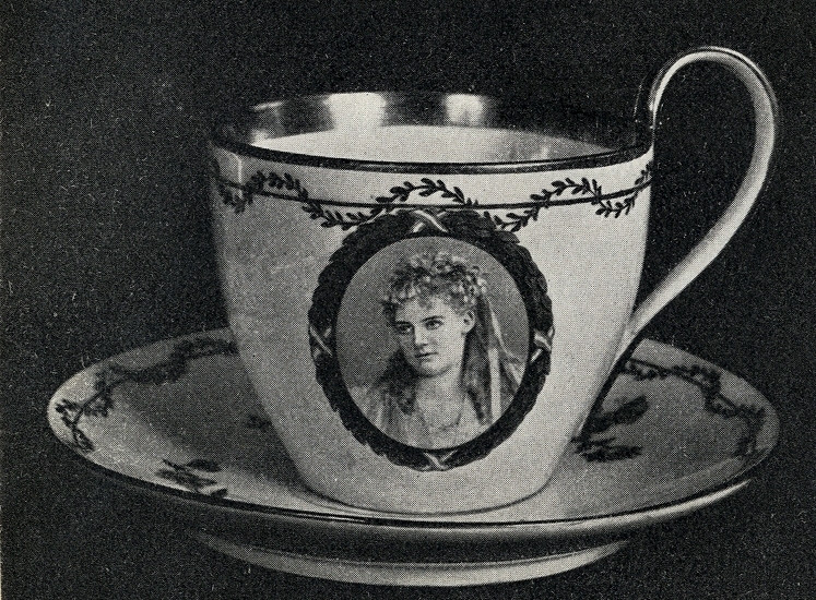 Koppen och fatet är vita med bladmönster. På mitten av koppen finns en bild på Christina Nilsson i oval ram.