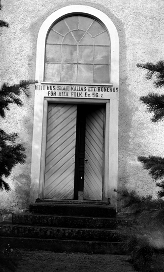 Foto på kyrkdörr med trappa och en text övanför dörren:
"Mitt Hus Skall Kallas Ett Bönehus För Alla Folk , Es 56:7."
Litt.: Smålandsposten 14/5 1932.