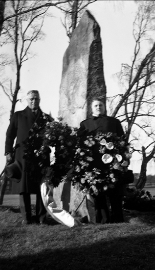 Foto på två män som står framför Per Henrik Lings minnessten med kransar i händerna.