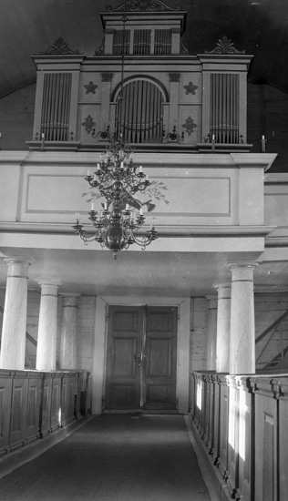 Kyrkläktare med kyrkorgel fotograferad från mittgången.  Över gången hänger en ljuskrona.