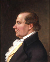 Portrett av Peder J. Cloumann. Profil. Mørk drakt, hvit skjorte med kalvekryss, lys gul vest.