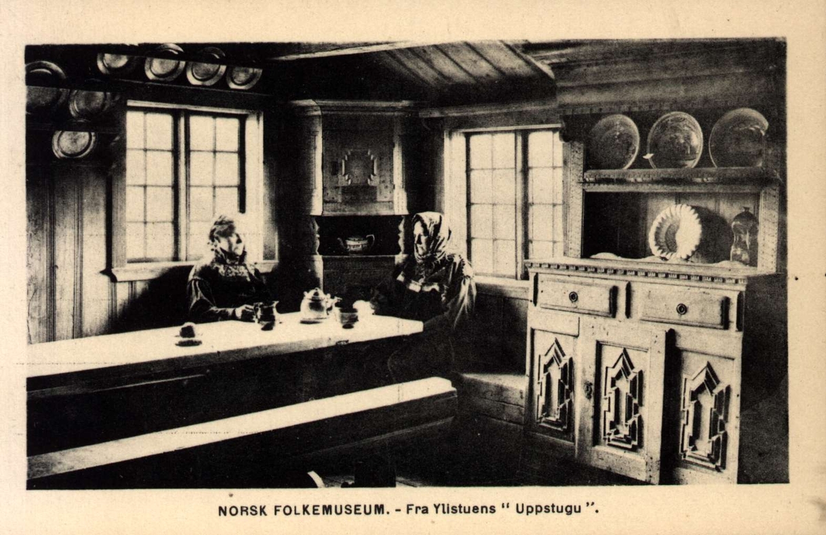 Postkort. Ylistuens "Uppstugu", 2 kvinner i bunader ved langbordet.Telemarkstunet, NF.