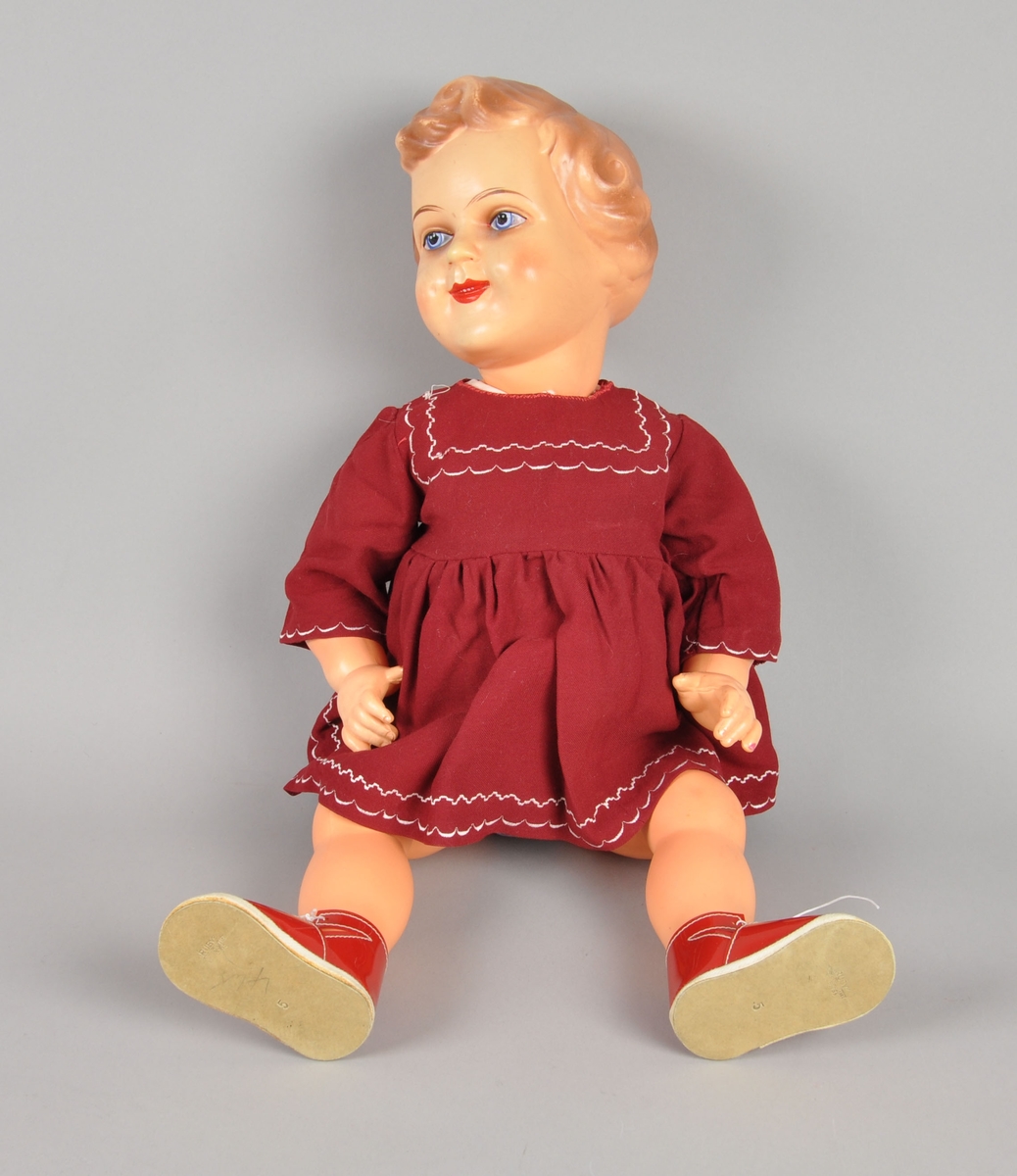 Dukke av celluloid. Dukken gikk under navnet "Gro-dukken). Dukken har påmalte øyne, munn, hår og kinn. Den er kledd i kjole, bukse, sko og undertøy.