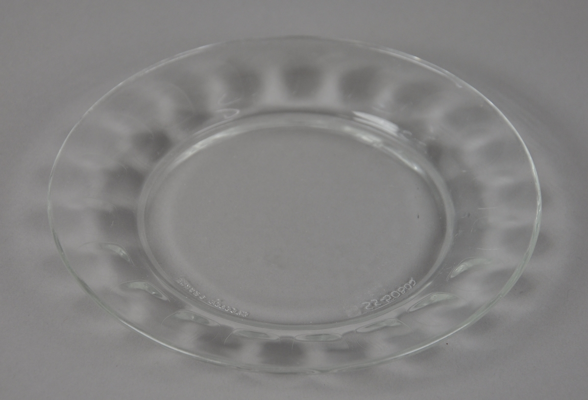 Asjett av glass med opphøyd kant. Fasettert mønster på kanten av asjetten,