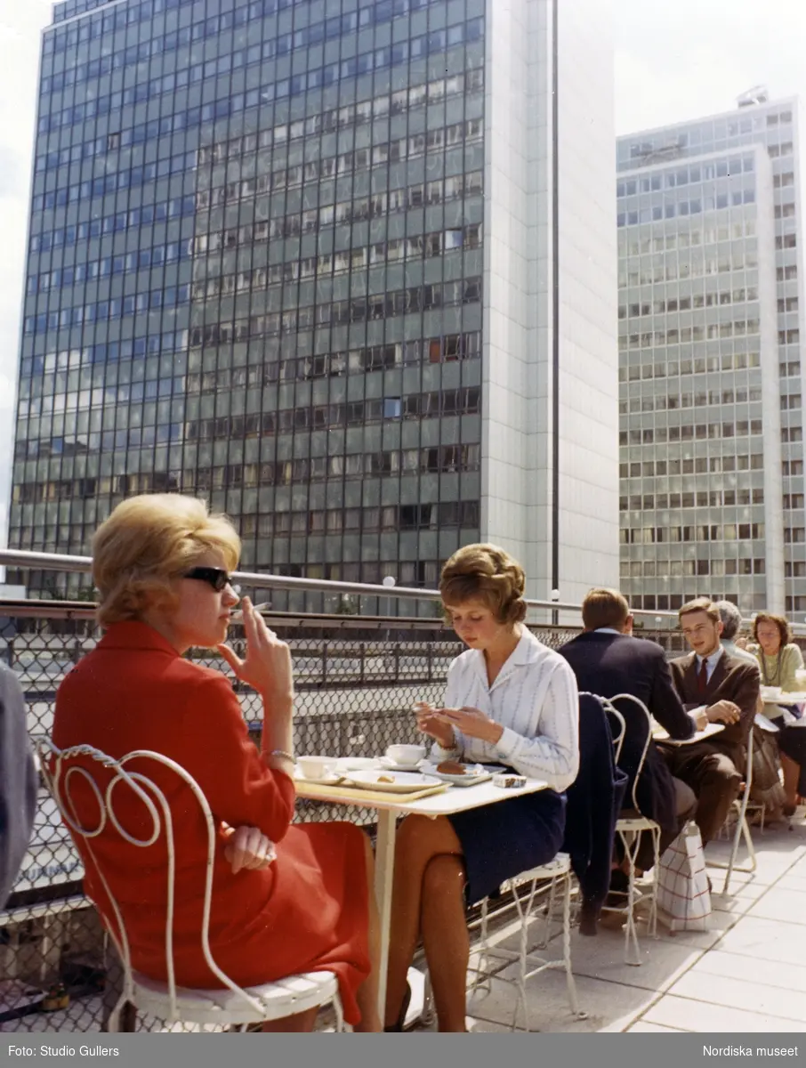 Stockholm. Cafégäster sitter vid bord på en uteservering. Hötorgsskraporna i bakgrunden.