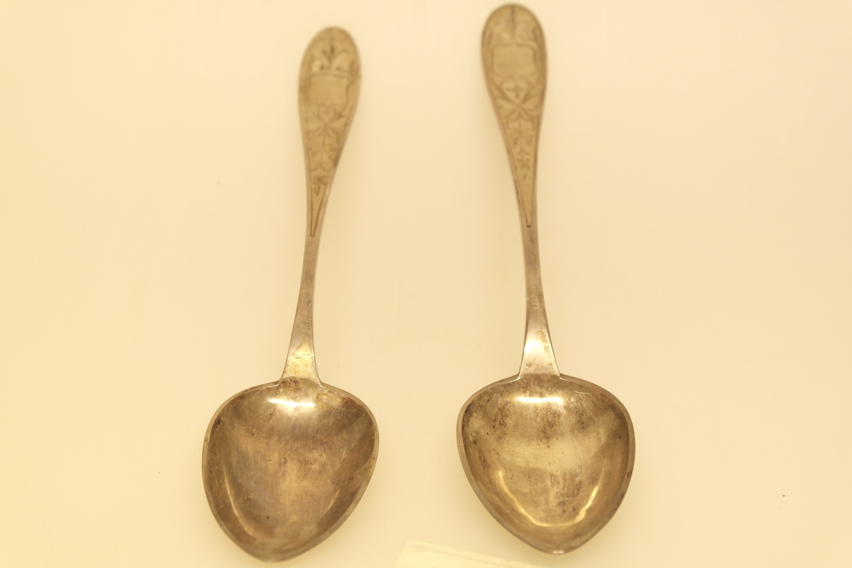 To spiseskjeer (a-b) i sølv. Inngravert opphøyet renessansemønster på skaftet. Stemplet på baksiden av skaftet.