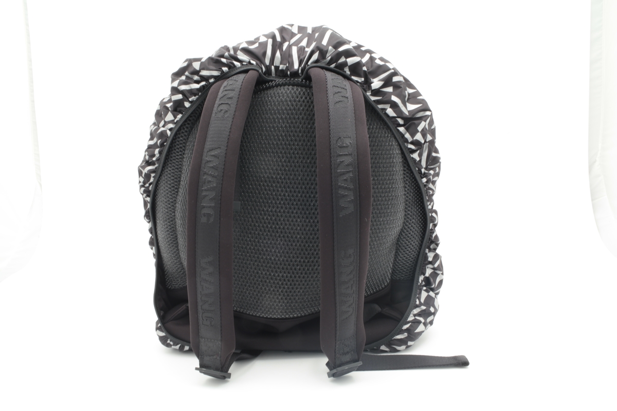 Liten sekk for trening. Sydd av nettstoff, der det ytre stoffet er laminert med flere lag nettstoff, og kjernen antagelig selvlysende, dvs av lysegrå refleksfibre. Sekken består av ett hovedrom og et lite ytterrom. Nedre del av både sekk og ytterrom er av tett neopren. Selve bunnen har en påsydd plate av gummi, med 4 "ben" i form av logoen "AW".  Innvendig bunnplate er imidlertid både bredere og lengre og av ukjente materiale. Sekken er flat nederst og buet i overkant, hovedrommet åpnes nesten helt ned i begge sider og lukkes med grov plastglidelås. Ytterommet åpnes i overkant og lukkes med tilsvarende glidelås. Innvendig er rommene fôret med et ekstra lag, enkelt nettstoff, og hovedrommet utstyrt med en ekstra lomme. Selene er regulerbare med spenner, er polstret, av neopren og utvendig forsterket med påsydde bånd av bevernylonlignende materiale ivevd "WANG" gjentatte ganger. Tilsvarende stropp øverst, til bæring i hånden. Under selefestene en ekstra lomme, lukket med samme grove glidelåstype. Nedi lommen ligger et påsydd regntrekk av tynt, vannavstøtende matriale, med påtrykt "AW" i et sammenhengende mønster utført i lysreflekterende trykkfarge over det hele. Med påsydd elastikk langs ytterkanten, kan trekket raskt tas ut og vikles omkring sekkens front og holde seg på plass i regnvær. Alle glidelåser er utstyrt med en "drastropp" av det sorte bondet ivevd WANG.