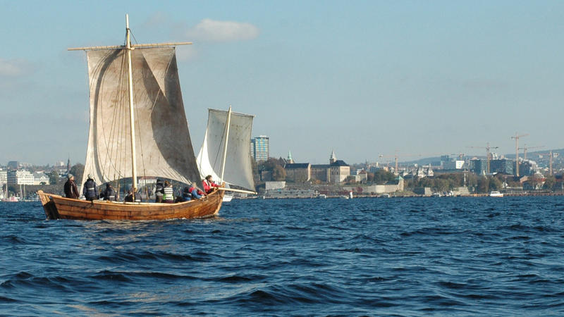 Trebåten Vaaghals på vannet med to seil, Oslo i bakgrunnen. Minst åtte personer ombord.