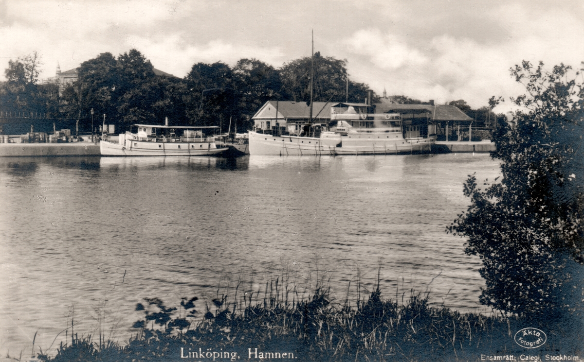 Bildtext: Linköping. Hamnen.
Hamnen sedd från öster, strax norr om järnvägsbron.
Hamnkontoret höger i bild.

Extern upplysning: Det lilla fartyget hette Maria och trafikerade sjön Roxen 1918-1926. Det större fartyget hette Trafik.
