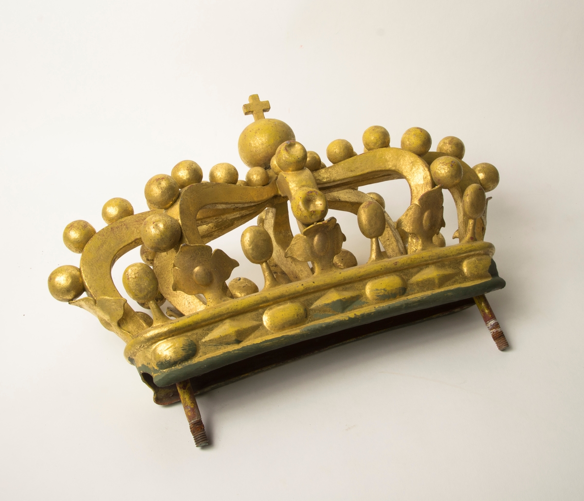 Ornament i form av en krona i förgylld metall. Kronan har två metallskruvar nedtill för anfästning. Förgyllningen har en bolus-färgad grundering.
