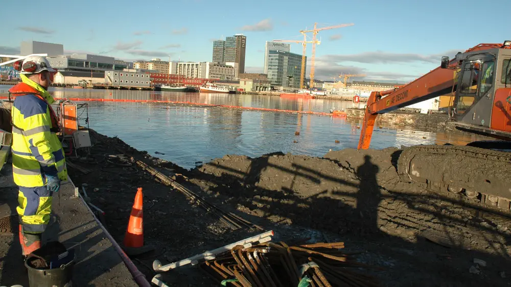 Arkeolog overvåker våtgraving på Senketunnelprosjektet. Oslo med Operaen i bakgrunnen.