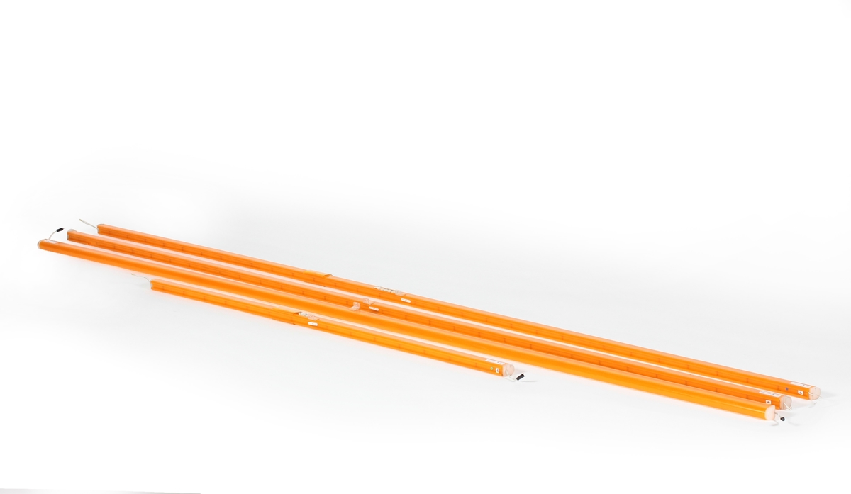 Oransje lysstoffrør, 4 stk., som er koblet sammen med små sammenkoblingsledninger. Lysstoffrørene har vært montert langs taket over bensinpumpene på bensinstasjonen