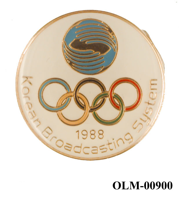 Rund sponsorpins med KBS sin logo fra Seoul'88 og de olympiske ringene i farver på hvit bakgrunn.