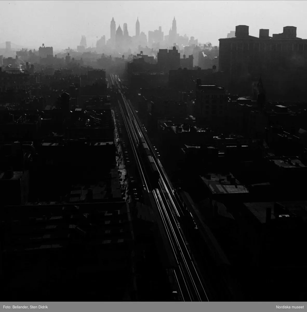Järnvägen skär genom Manhattan. Rälsen blänker i motljus. Skyline.
