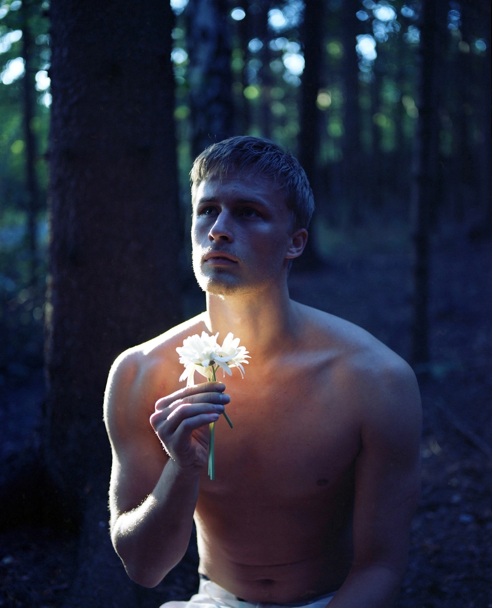 Fotografiet viser en ung mann med en hvit blomst som han holder i hånden.