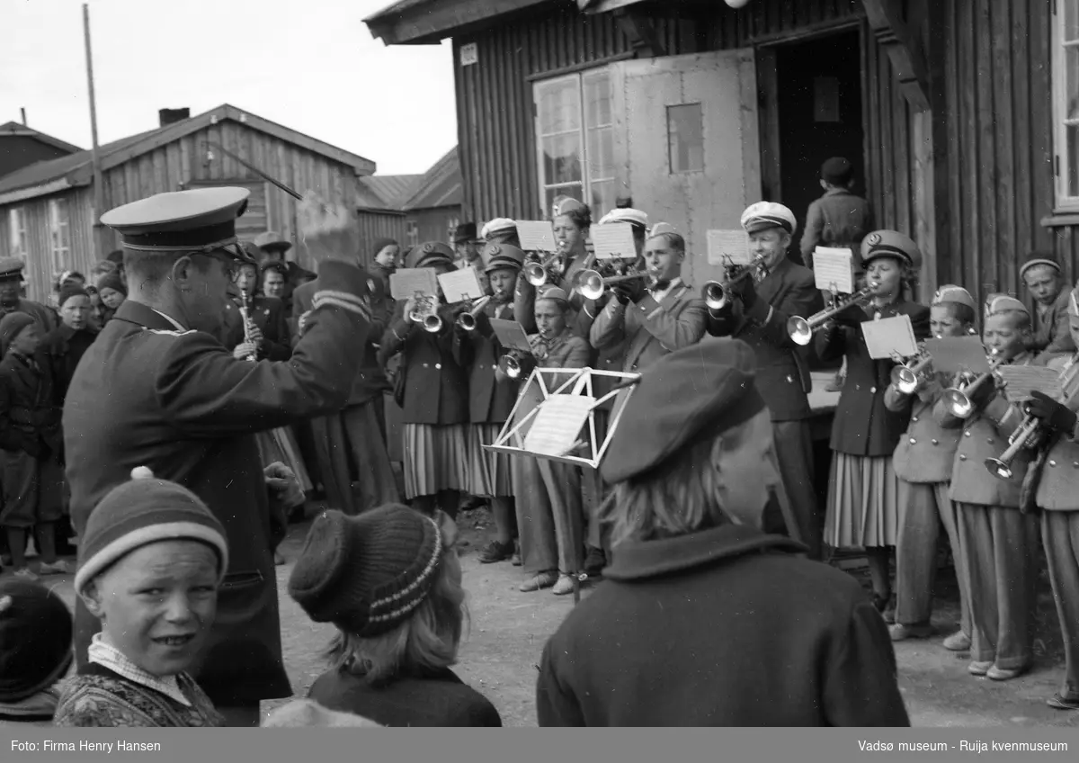 Vadsø sentrum 17. mai 1951. Musikkorpset står oppstilt og spiller utenfor postbrakka. Det er Vadsø jentekorps og guttemusikken som spiller.