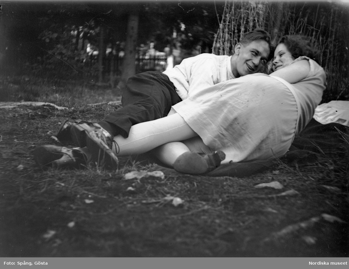 Ett par, John och Märta Spång, ligger i gräset intill ett träd.