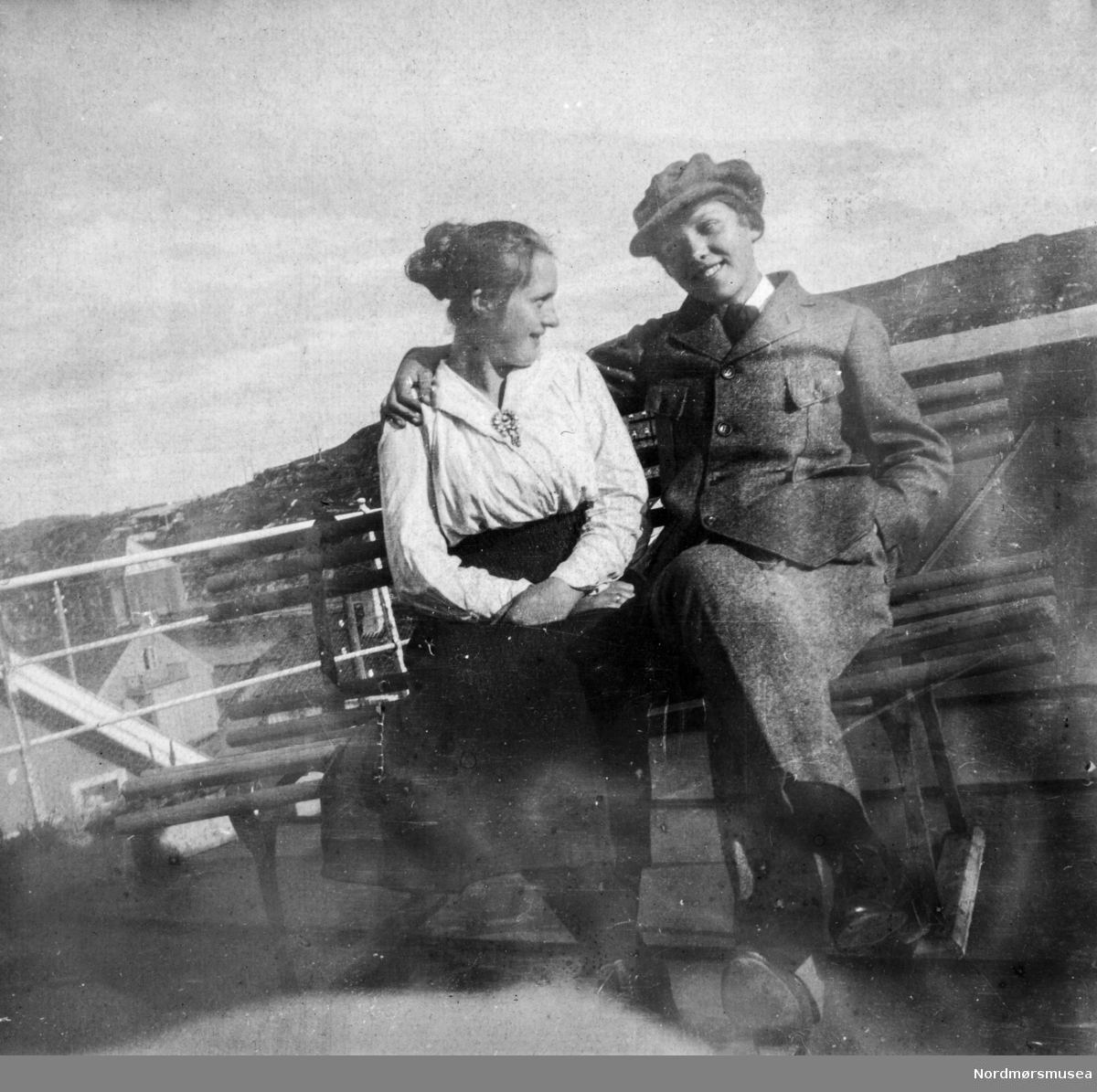 Gruppebilde av to personer sittende sammen. Bildet er trolig fra Kristiansund omkring 1918-1920 og de vi ser på bildet er sannsynligvis fra Williams-familien. Fra et fotoalbum tilhørende Ellinor Williams-Phakdikun (1905-1963). Fra Nordmøre museums fotosamlinger.
