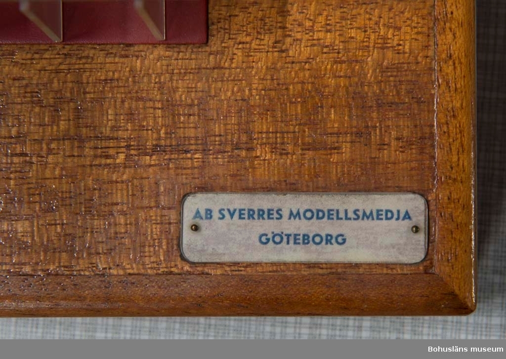 Modell av sektion till bulklastbåt stående på en träsockel.
Färgen är röd och grön + genomskinlig plast.
Märkningar på båda sidor på sockeln: "AB Sverres modellsmedja Göteborg".