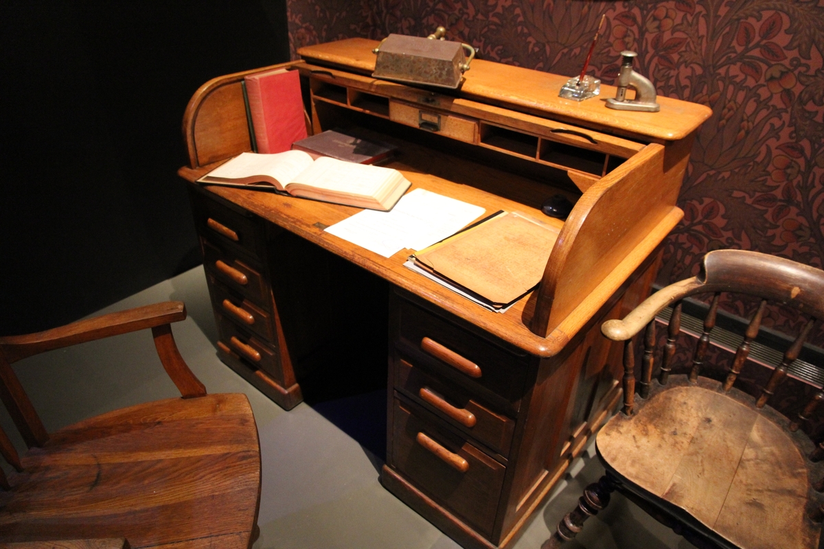 Skrivebord med sjalusi til å lukke med. 3 skuffer på venstre side. I fire deler, Øverste del med sjalusi, hyller og skriveflate hviler på to skuffeseksjoner som kobles sammen av en bakplate.