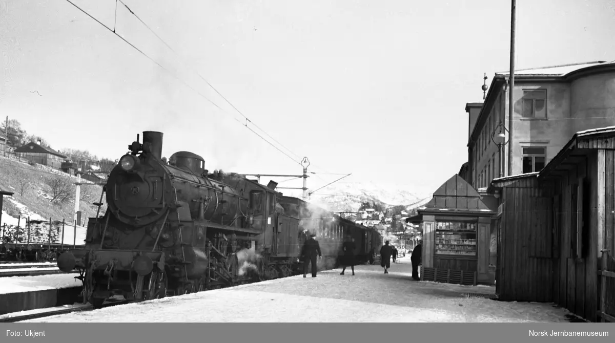 Voss stasjon med reisende og damplokomotiv foran persontog i spor 1