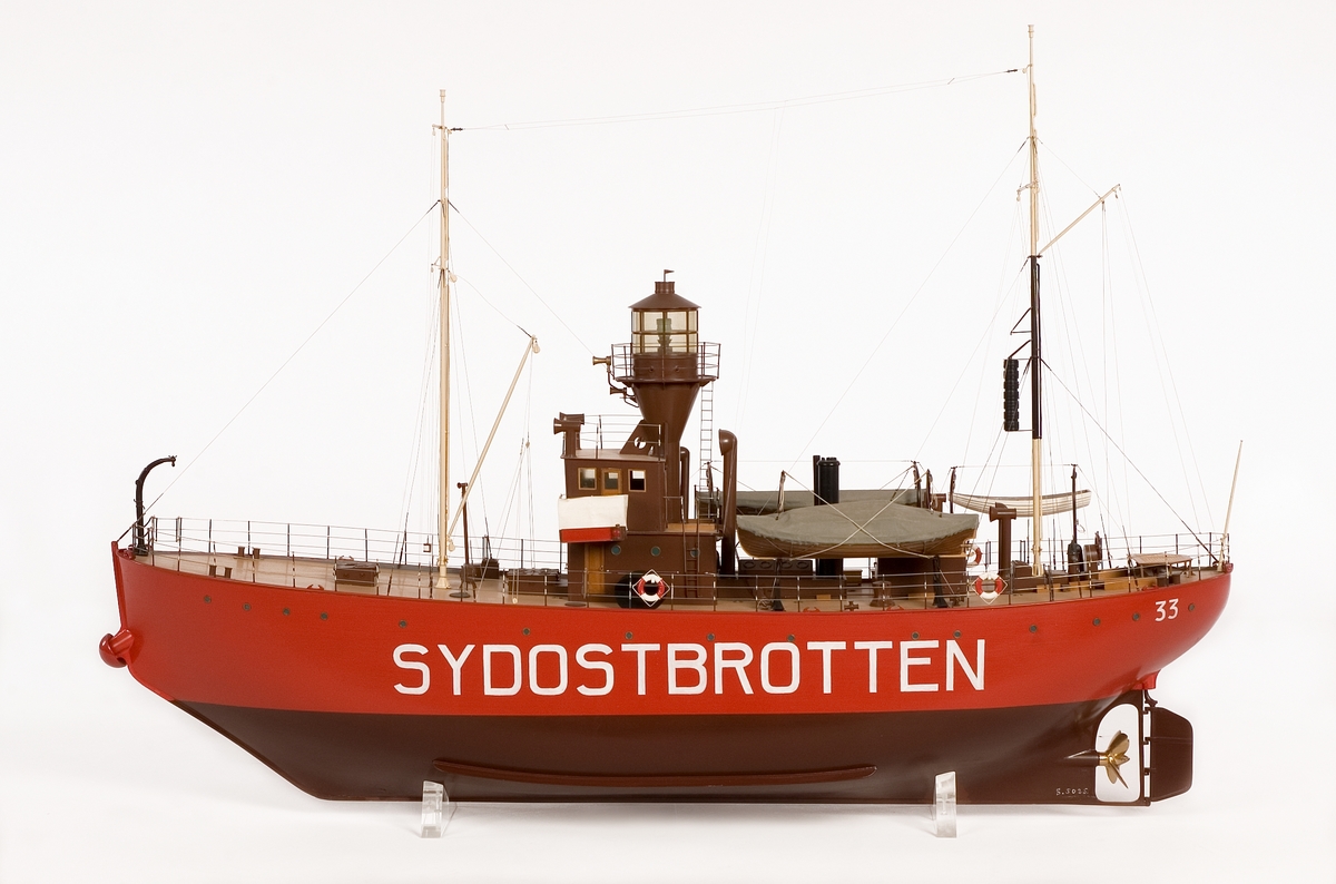 Fartygsmodell av fyrskeppet SYDOSTBROTTEN styrbords sida öppen, visande inredning. Fyrtorn med plattform runt lanterninen. Två master, tre båtar och ett skålankare i centralt stävklys.