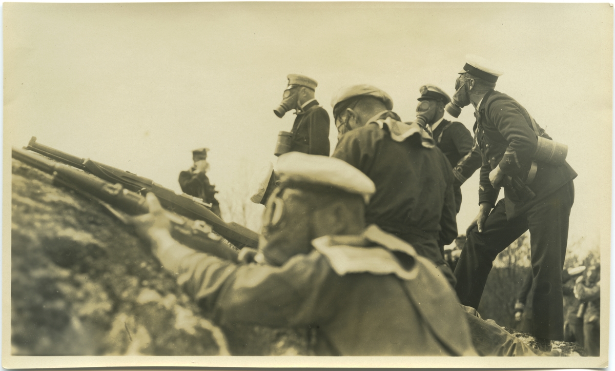 Officerare och manskap iförda gasmask under stridsövning. Av andra bilder i Bergers samling framgår att denna bild tagits under landstigningsövning med besättningen från pansarskeppet SVERIGE på Stabbo i Stockholms södra skärgård 1929.
