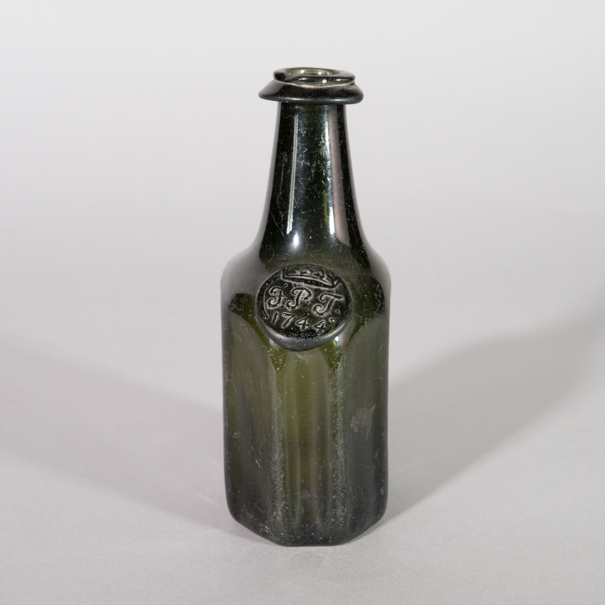 Flaska av grönt glas. 8-kantig kropp, axlar och rund hals. Sigill.