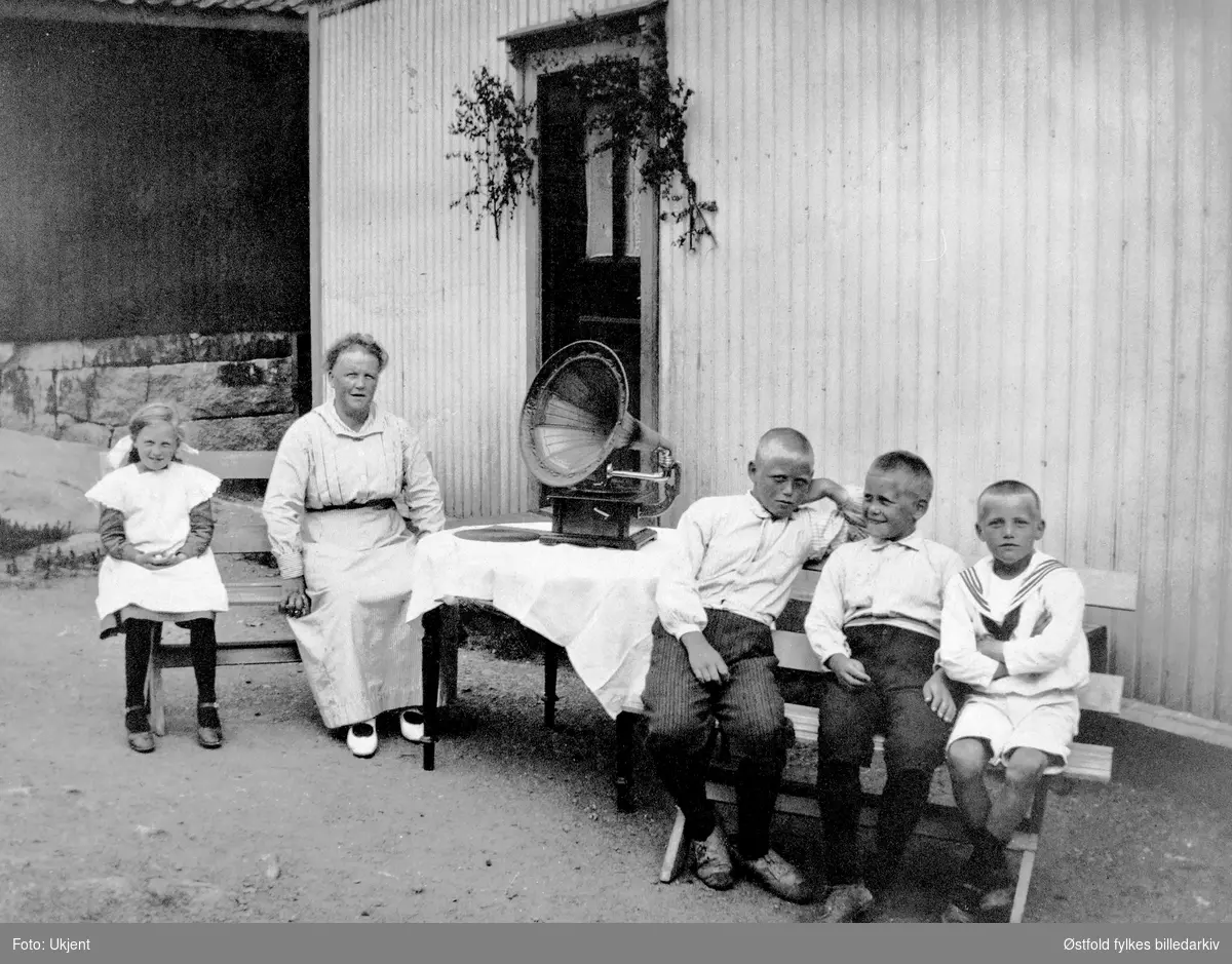 St. Hansfeiring, bruksbebyggelsen, Øyenkilen i Onsøy 1919. 
Tre brødre Kile, deres mor og 11 år gamle Astrid Lilly Hansen sittende utenfor bygning ved bord med tut- grammofon.