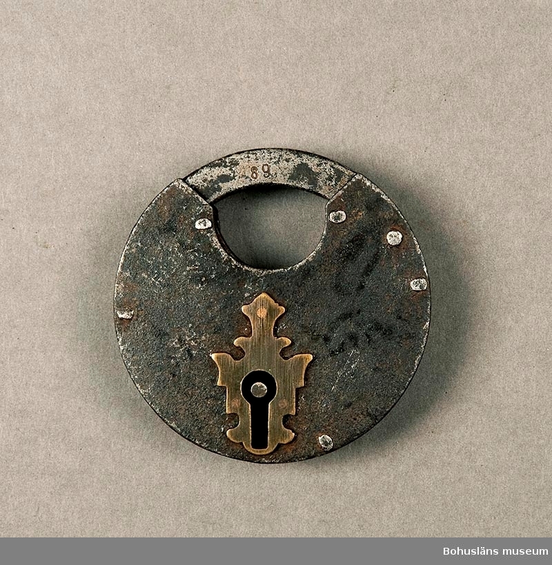 Ur handskrivna katalogen 1957-1958:
Hänglås m. nyckel
Låset (A), cirkelrunt, D. 8,7 cm; järn, nyckelhålsskylt av mässing; "89". Nyckeln (B) L. 5,8 cm. Föremålen hela.