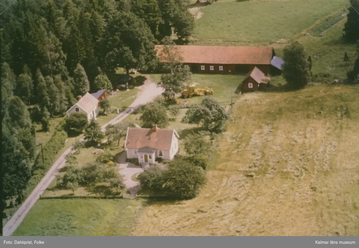 En villa, ekonomibyggnad och jordbruksmaskin vid åkermarker i Madesjö.
