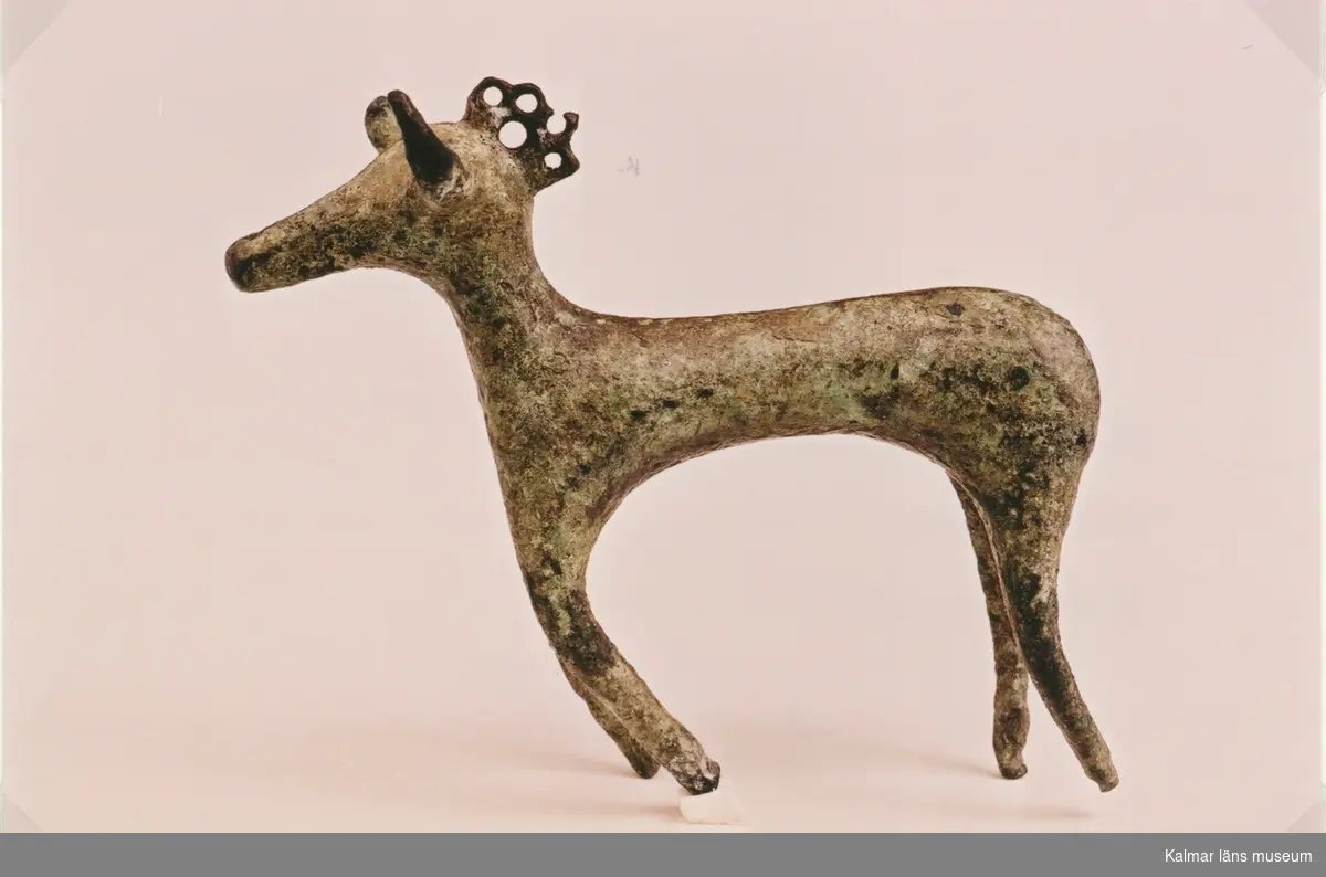 Tjur eller hjortstatyett av brons, kronprydd. Fynd vid arkeologisk undersökning 1991-92 i Gräsgård sn, Solberga 4:5/2, fornl.nr 81. 

Höjd 7 cm.
