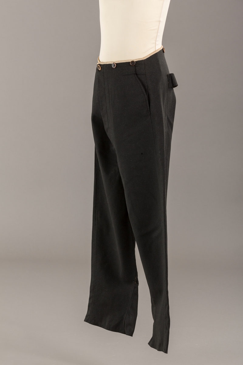 Form: Bena utvidet nederst. Lerretskant rundt livet, spensel i ryggen, mangler spenne i sepnsel?
Delvis foret. To lommer. 5 knapper, mangler en knapp.