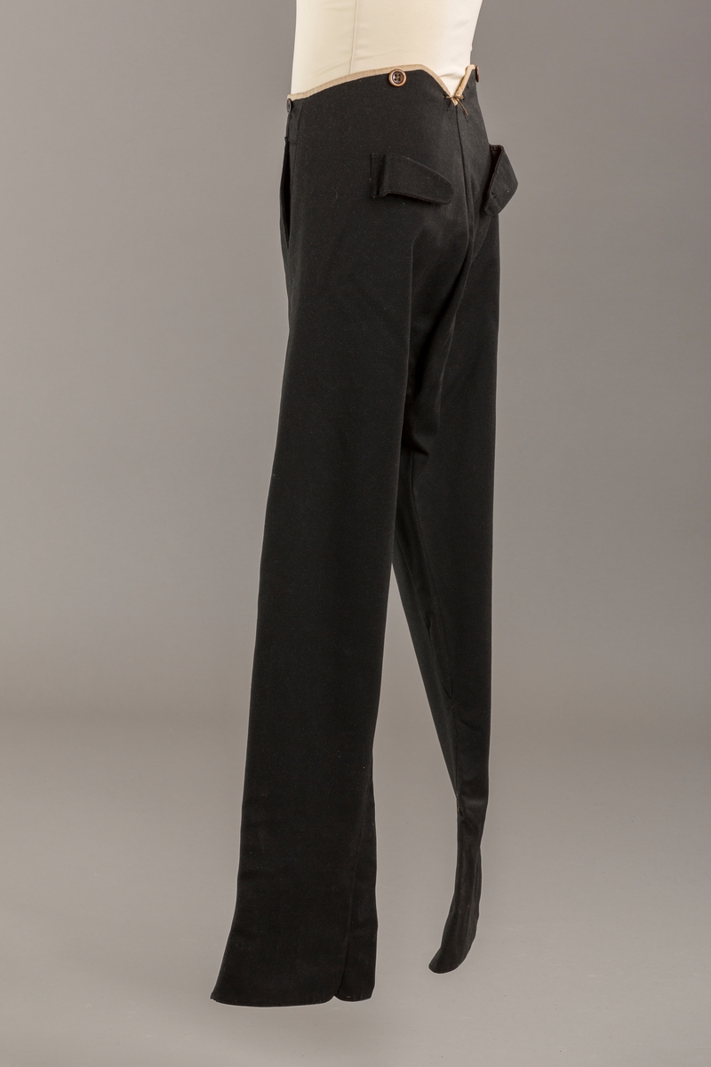 Form: Bena utvidet nederst. Lerretskant rundt livet, spensel i ryggen, mangler spenne i sepnsel?
Delvis foret. To lommer. 5 knapper, mangler en knapp.