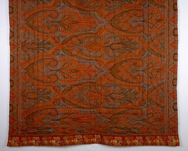 Vaddstickat täcke, sytt av en stormönstrad "persisk" sjal av ull och bomull i rött, gult, brunt och blått. Baksidan är av bomullstyg.