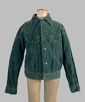 Blåaktigt grön jacka sydd av manchestertyg. Modellen är sydd med ok, rund halsringning, knäppning mitt fram samt linning längs nedre kanten. Ärmen avslutas med en linning. Runt halsringningen är en krage med spetsiga snibbar fäst. Jackan är av märket "Waquero".
Anm. enl liggaren "Tillhör 1974 års tonårsmode, men användes fram till 1977"