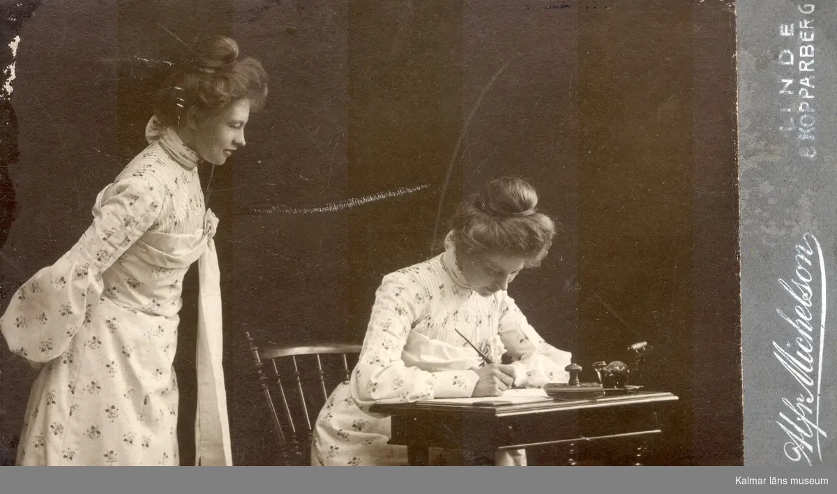 Visitkort, dubbelporträtttav Ellen Warnholm i vit klänning med blommor, dels sittande vid bord, dels stående i profil tittandes på sig själv.