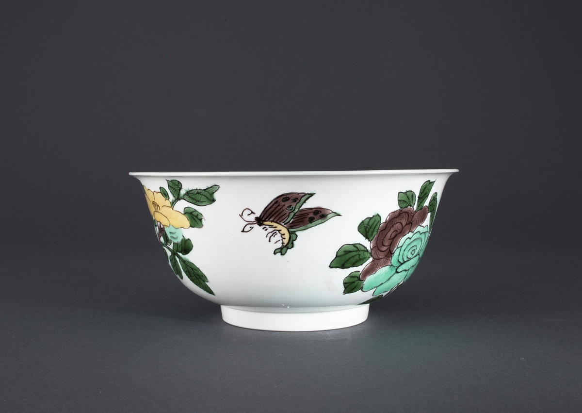 Oveglasur på hvit bakgrunn. Overglasurdekor: To grupper med  hibiskusblomster i pastell lavendlgrå, pastell turkis og pastell sitrongul med blader i en kraftig grønnfarge. Mellom de to blomstergruppene er sommerfugl som reflekterer fargene i blomstene. I godset under hver blomstergruppe er det innrisset en drage.